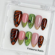 Monarch Meadow Magic press-on nail set arranged in a Veloura Nails display case