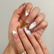 Amber Ghost Lantern press-on nails with white ghosts and amber pumpkin details shown on hand
