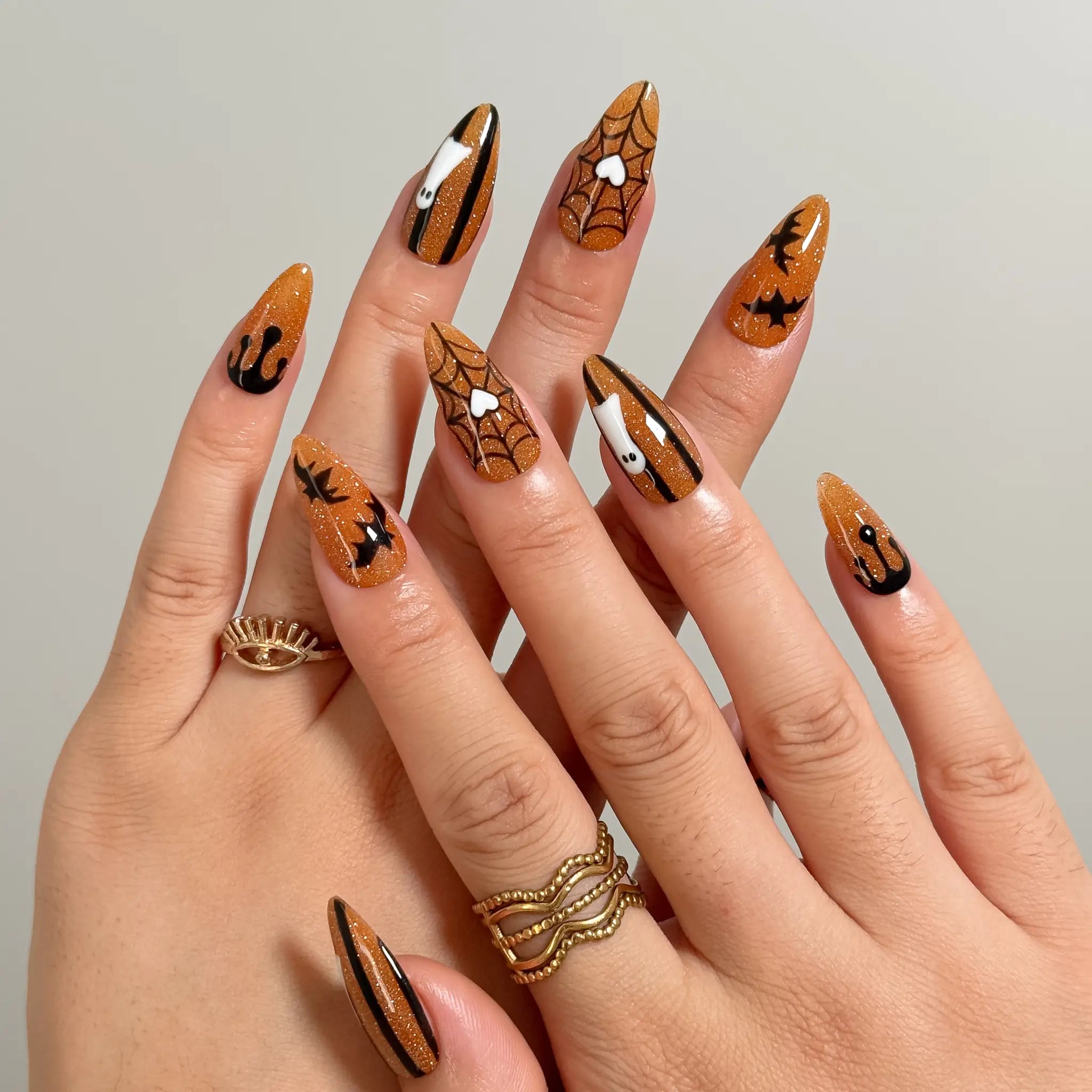 Haunted Amber Web long stiletto press-on nails with orange glitter, black webs, bats, and ghosts shown on hand
