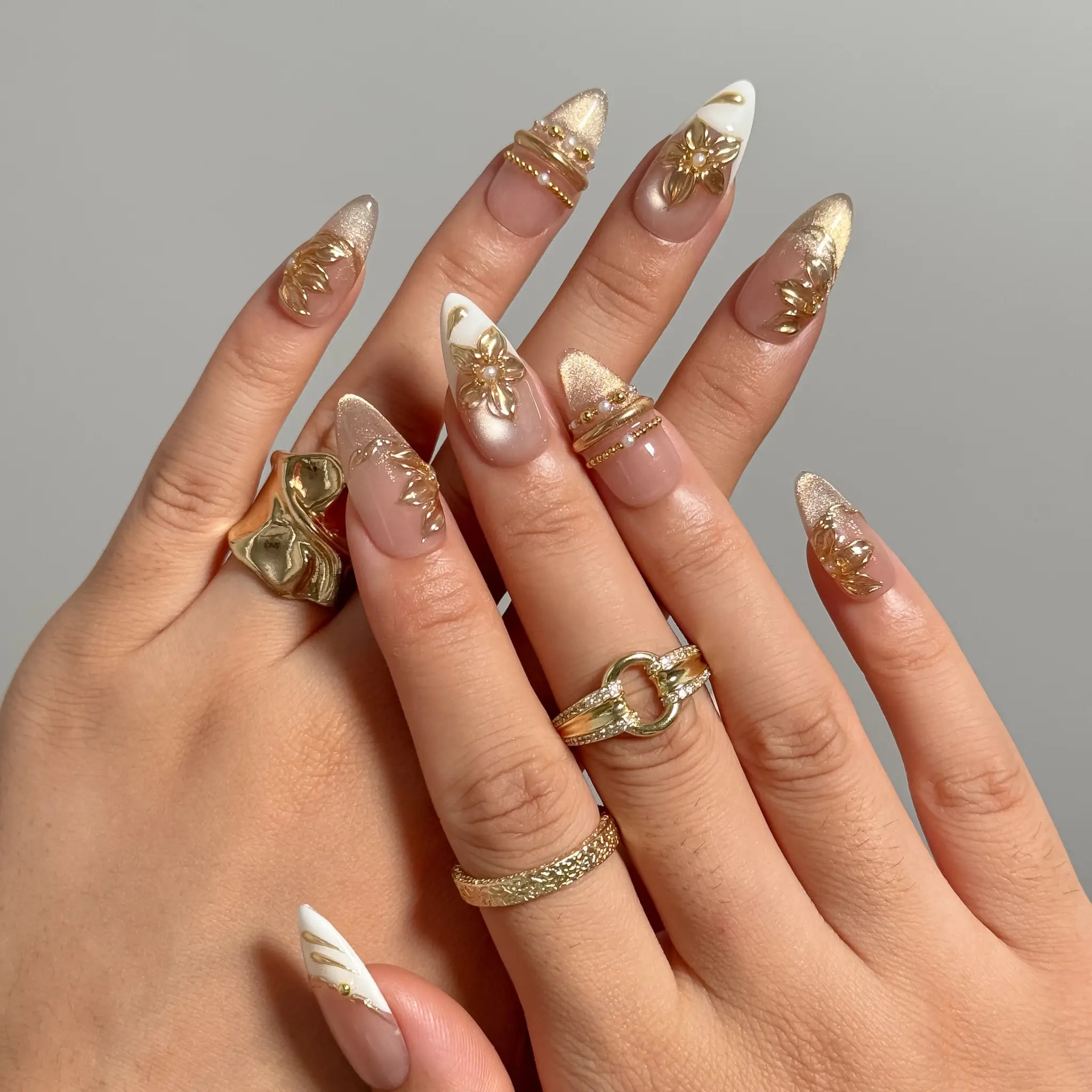 Gilded Magnolia Veil long almond press-on nails with raised gold flowers and white French tips shown on hand