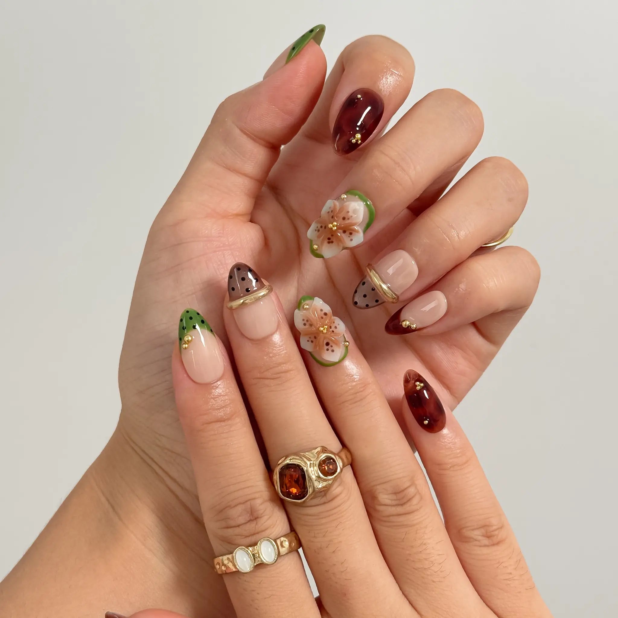 Orchard Truffle Bloom long almond press-on nails with green tips, brown accents, sculpted flowers, and gold details shown on hand
