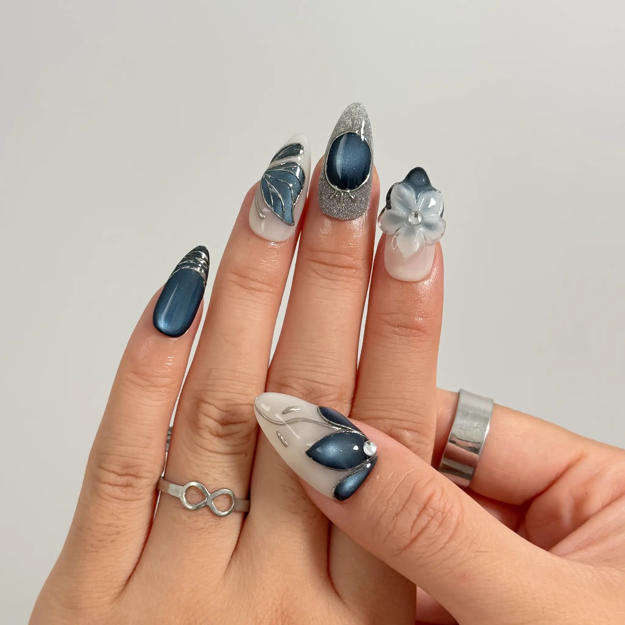 Midnight Petal Sonata long almond press-on nails with blue cat-eye accents, silver shimmer, and sculpted flowers shown on hand