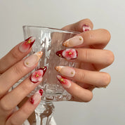 Crimson Bloom Compass long almond press-on nails with raised crimson flowers, gold starbursts, and nude bases shown on hand