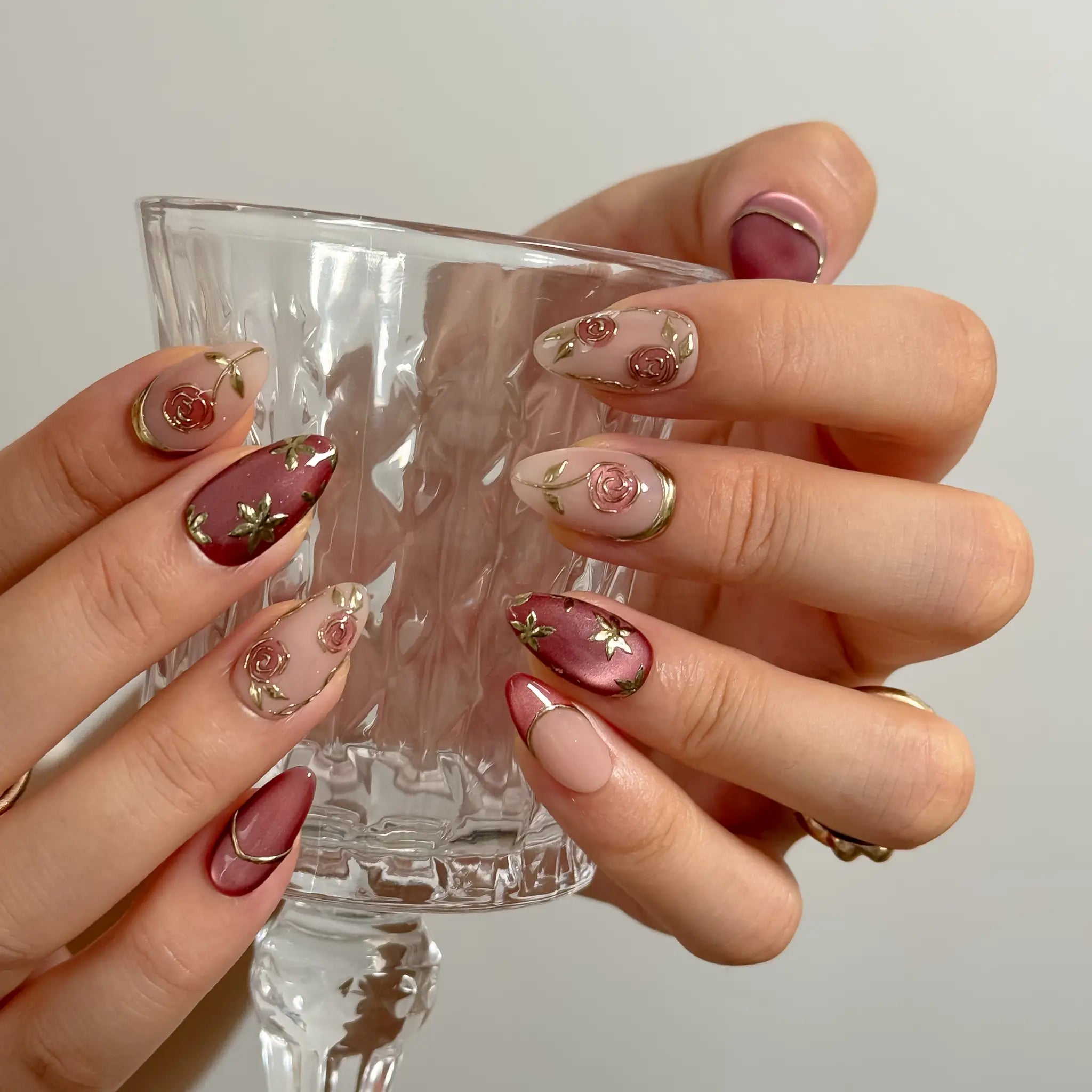 Rosewood Garden Glow long almond press-on nails with raised rose motifs and gold trim shown on hand