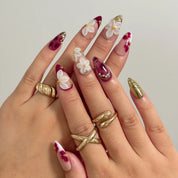 Burgundy Petal Heirloom long almond press-on nails with sculpted white flowers and gold accents shown on hand