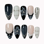 Midnight Alloy Bloom: black, nude and silver-tone almond press-on nails with raised gray flowers and studded tips, set arranged on a pale background.