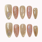 Daphne’s Golden Laurel: nude and gold-toned almond press-on nails with iridescent flakes and raised metallic textures, arranged on a pale background.