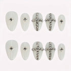 Divine Frost: white almond press-on nails with silver-toned crosses and clear gem accents, arranged on a pale background.